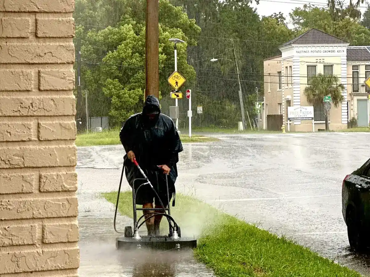 Technician surface cleaning the entry walkway of a brick office building in the rain
