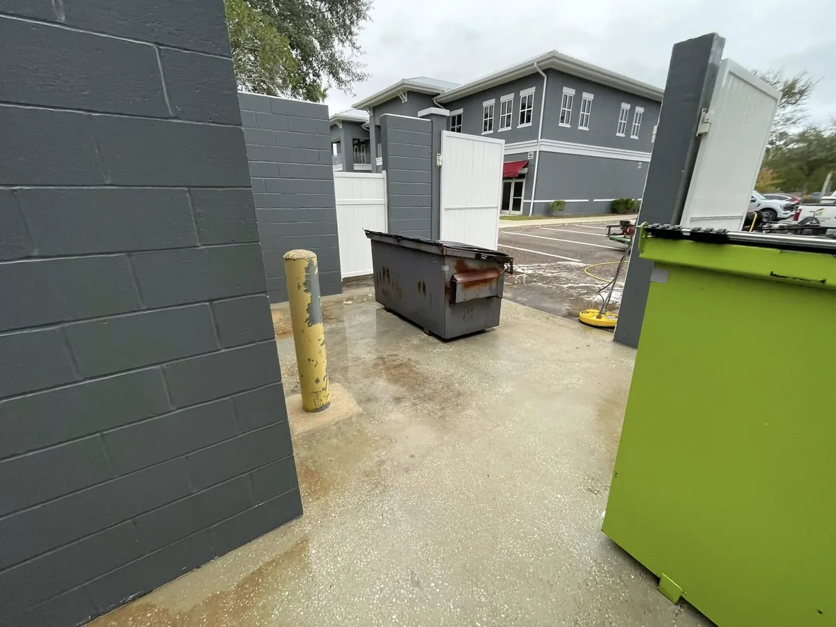 Dumpster enclosure and service area concrete cleaned behind a retail property