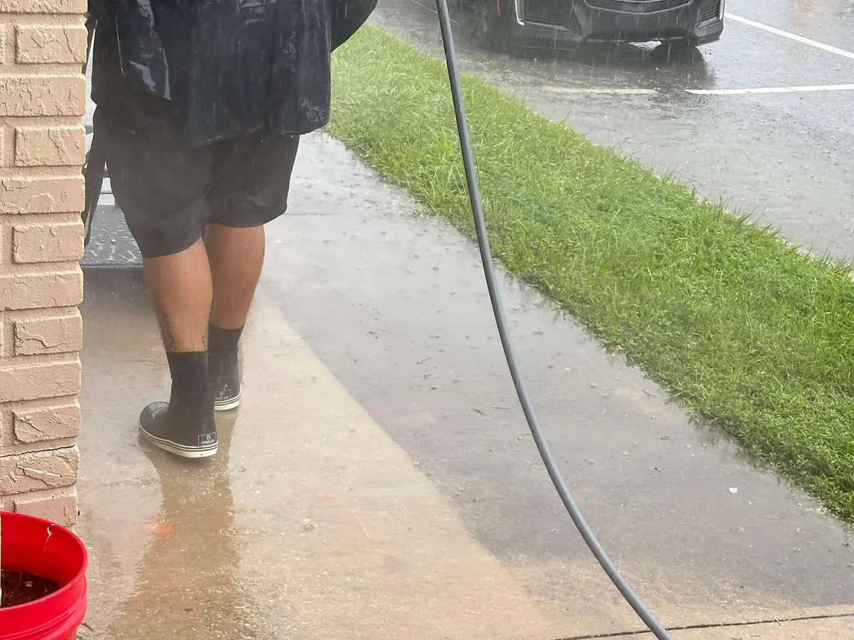 Technician surface cleaning a concrete walkway in the rain at a St. Augustine property